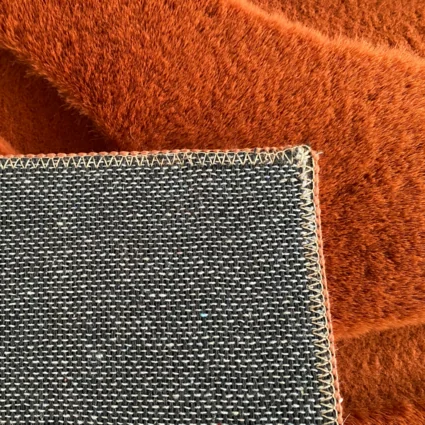 Detail koberca s tehlovou farbou a 3D vzorom, zobrazenie okraja a textúry materiálu.